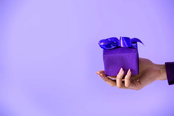 Vue recadrée sur une main féminine tenant un cadeau violet, isolée sur ultraviolet — Photo de stock