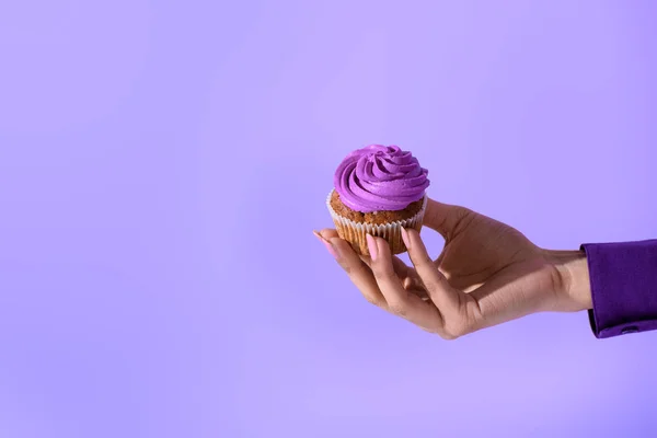 Обрезанный вид на женскую руку с кексом с фиолетовой глазурью, изолированный на ультрафиолетовом — стоковое фото