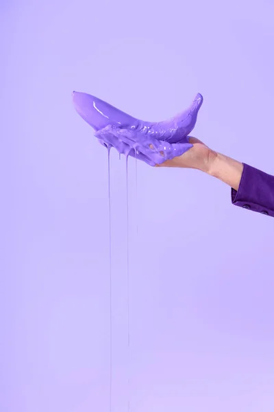 Vista recortada en la mano femenina sosteniendo plátano en pintura púrpura, aislado en ultravioleta - foto de stock