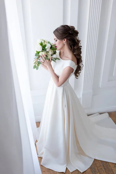 Mariée élégante en robe blanche traditionnelle reniflant bouquet de mariage — Photo de stock