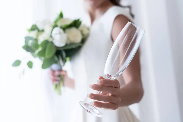 Foco seletivo da noiva com buquê de casamento segurando copo de champanhe vazio — Fotografia de Stock