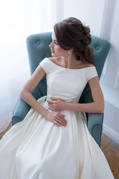 Attractive young bride in wedding dress sitting in armchair — Stock Photo