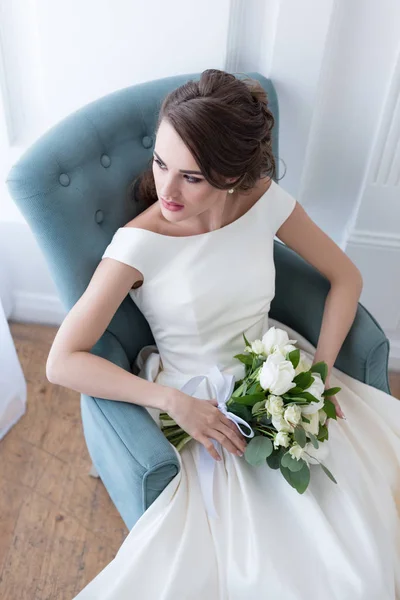 Attraktive Braut mit Brautstrauß im Sessel sitzend — Stockfoto