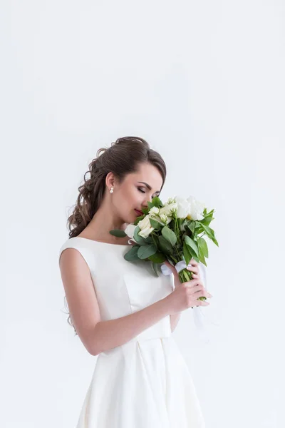 Привлекательная невеста с закрытыми глазами нюхает свадебный букет, изолированный на белом — стоковое фото