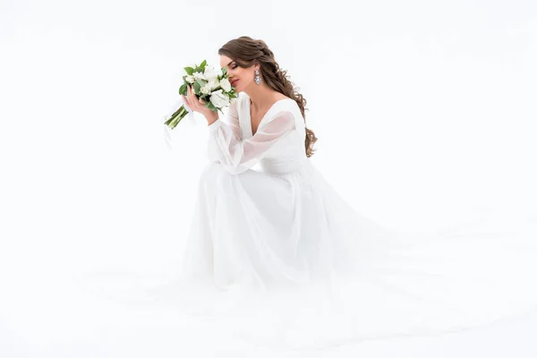 Happy bride in traditional dress sniffing wedding bouquet, isolated on white — Stock Photo