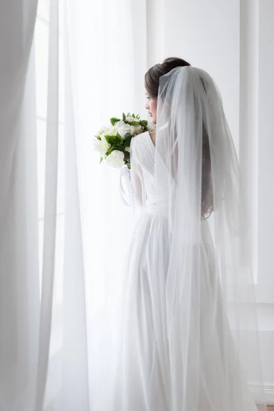 Back view of brunette bride in wedding dress with traditional veil and bouquet — Stock Photo