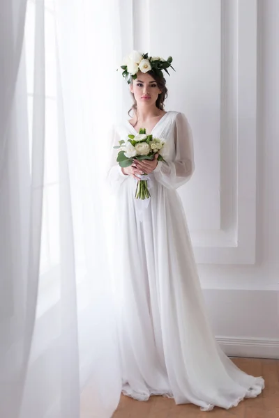 Atractiva novia en vestido tradicional y floral corona celebración de ramo de boda - foto de stock