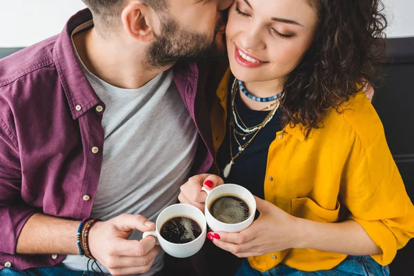 Jeune homme embrassant sa petite amie pendant qu'ils tiennent des tasses à café — Photo de stock