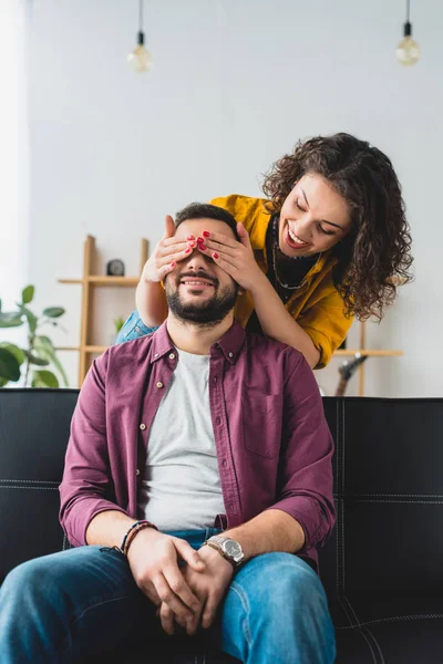 Sonriente joven mujer cerrando los ojos de su novio - foto de stock