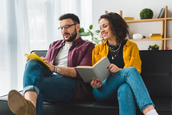 Junges Paar sitzt und liest Bücher auf Ledercouch — Stockfoto