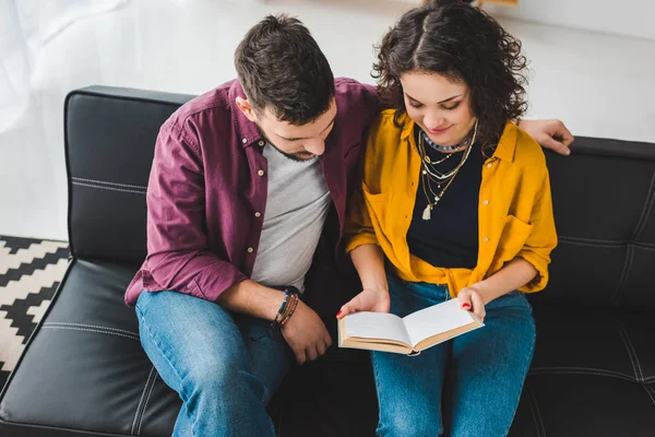 Blick aus der Vogelperspektive auf ein junges Paar, das auf der Couch sitzt und Buch liest — Stockfoto