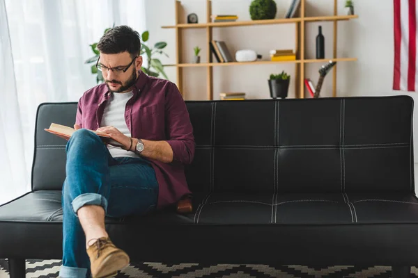 Front view of male in glasses reading book on couch — Stock Photo