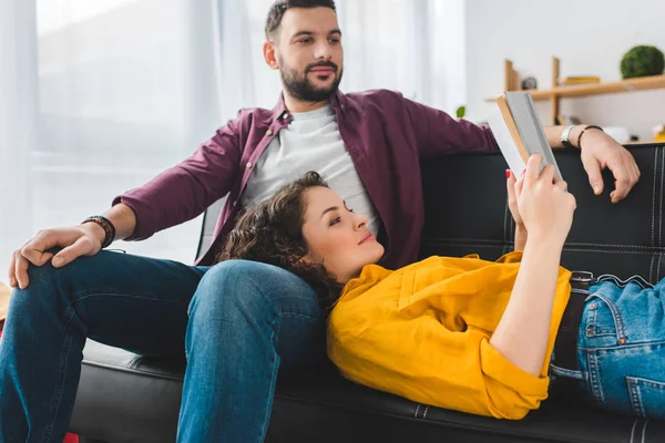 Mujer acostada sobre las rodillas de su novio y leyendo el libro - foto de stock