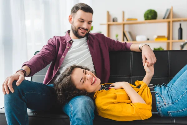 Mujer sonriente acostada sobre las rodillas de su novio y sosteniendo su mano - foto de stock