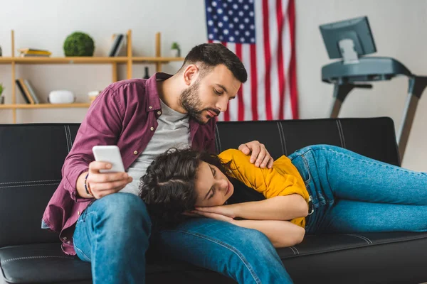 Homme utilisant smartphone avec petite amie endormie sur ses genoux — Photo de stock