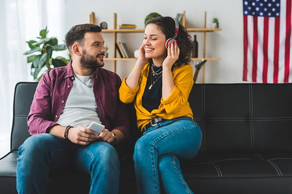 Mann hält Smartphone in der Hand, während seine Freundin Musik im Handy hört — Stockfoto