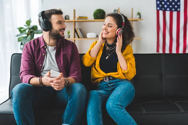 Young couple listening music in headphones and sitting on couch — Stock Photo
