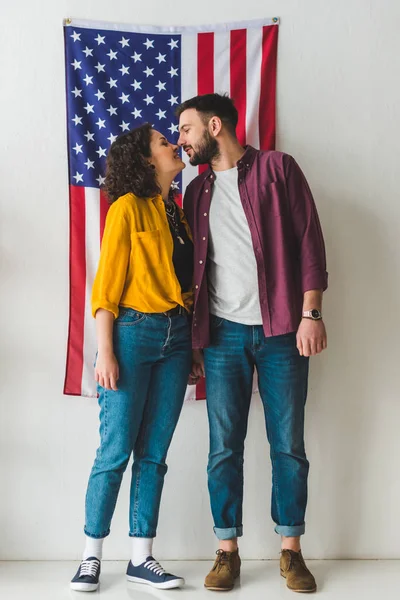 Jeune couple debout devant le mur avec drapeau américain — Photo de stock