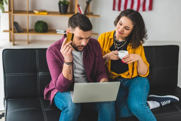 Uomo in possesso di carta di credito con computer portatile in ginocchio mentre la donna in possesso di una tazza di caffè — Foto stock