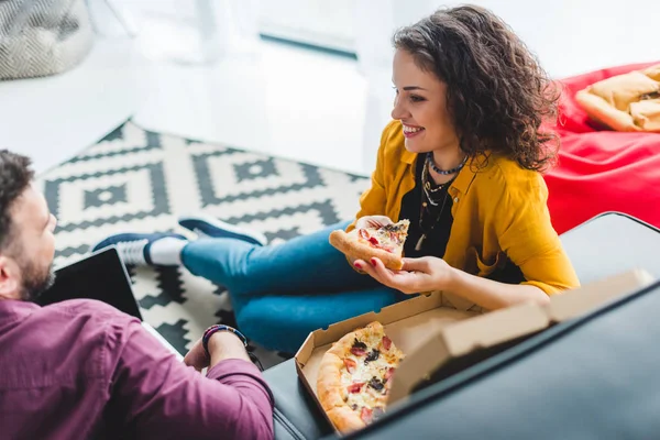 Vue latérale du couple mangeant de la pizza et assis sur le canapé — Photo de stock