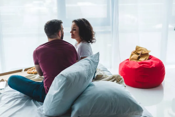 Rear view of young couple sitting on bed with pizza box — Stock Photo