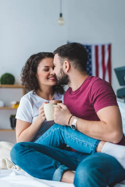 Side view of young kissing couple holding cups — Stock Photo