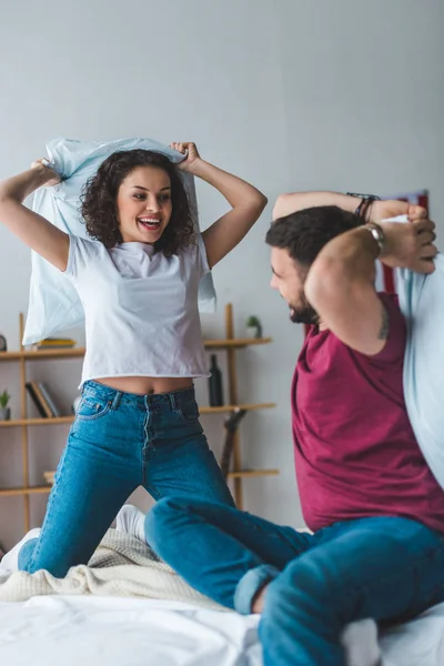 View of smiling couple fighting by pillows on bed — Stock Photo