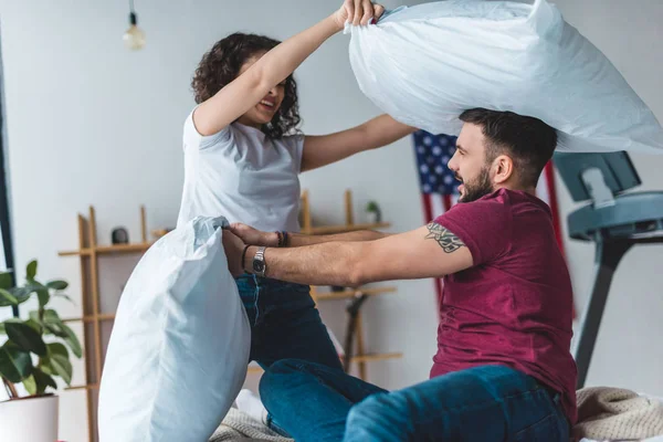 Vista lateral do jovem casal lutando por travesseiros na cama — Fotografia de Stock