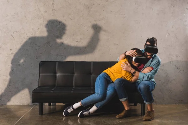 Ombre de l'homme tenant couteau et couple en réalité virtuelle casque sur le canapé — Photo de stock