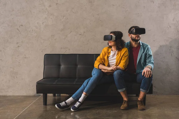 Casal sentado no sofá e usando fone de ouvido realidade virtual — Fotografia de Stock