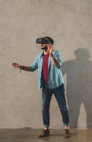 Jovem de pé na frente da parede e usando fone de ouvido realidade virtual — Fotografia de Stock