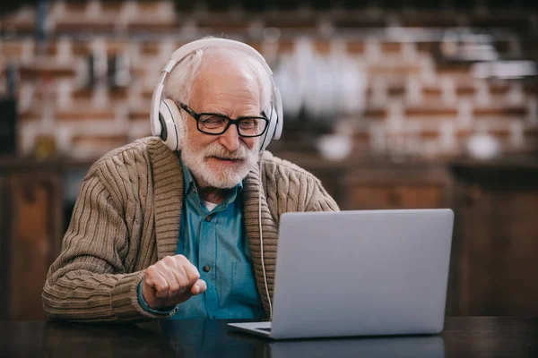 Homem sênior em fones de ouvido usando laptop — Fotografia de Stock