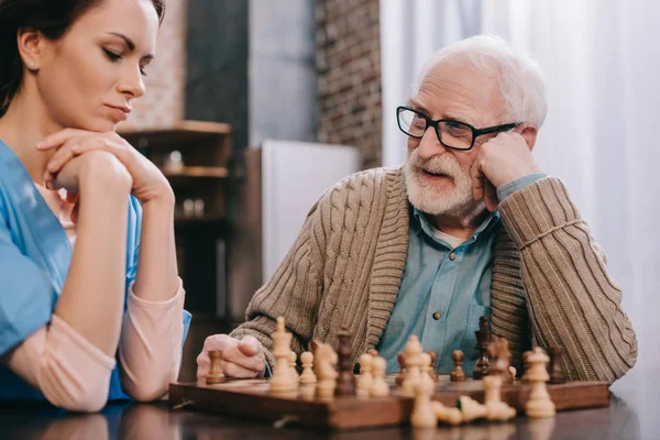 Infirmière réfléchie et vieil homme jouant aux échecs — Photo de stock