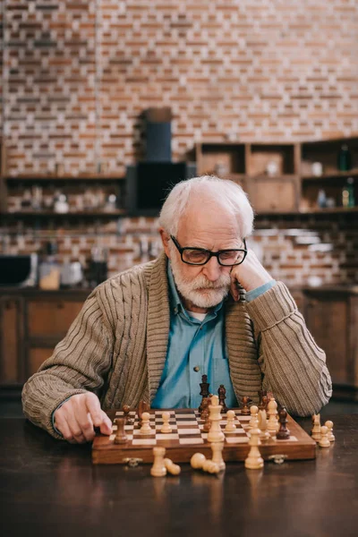 Задумчивый старик по шахматной доске — стоковое фото