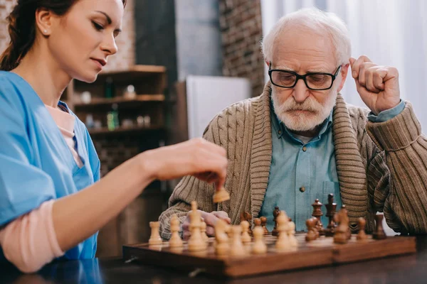Enfermeira e homem idoso jogando xadrez — Fotografia de Stock