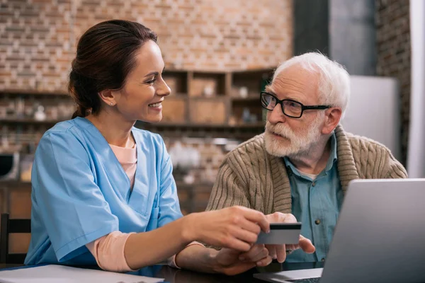 Infirmière aidant le patient âgé à utiliser un ordinateur portable et une carte de crédit — Photo de stock