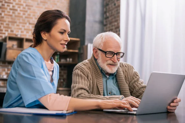 Медсестра сидит со старшим мужчиной с ноутбуком — Stock Photo