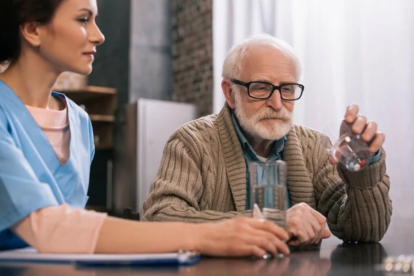 Nurse by senior man taking medications — Stock Photo