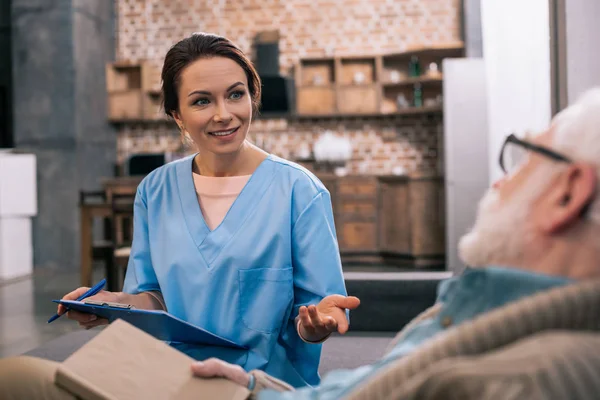 Elder man looking at nurse writing down medical complaints — Stock Photo