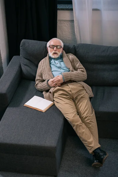 Старший мужчина спит на диване с книгой — стоковое фото