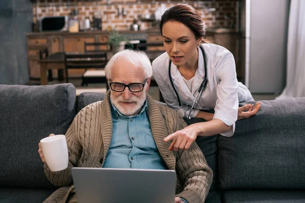 Doctor pointing at laptop in senior patient hands — Stock Photo