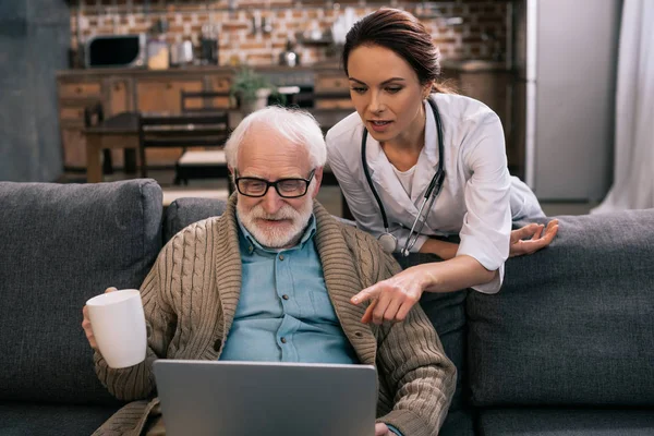 Medico che indica il computer portatile nelle mani dei pazienti anziani — Foto stock