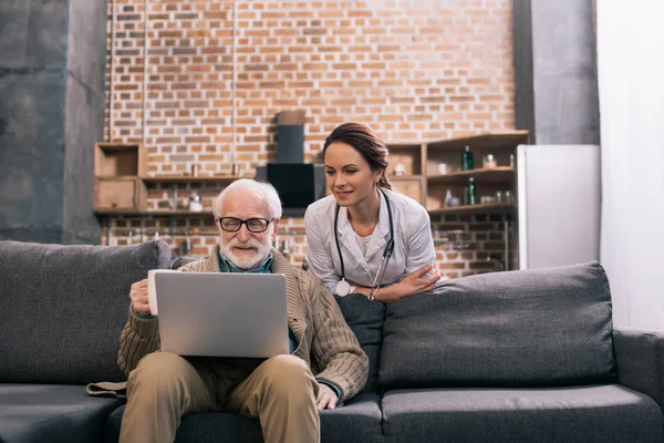 Médecin regardant ordinateur portable dans les mains des patients âgés — Photo de stock