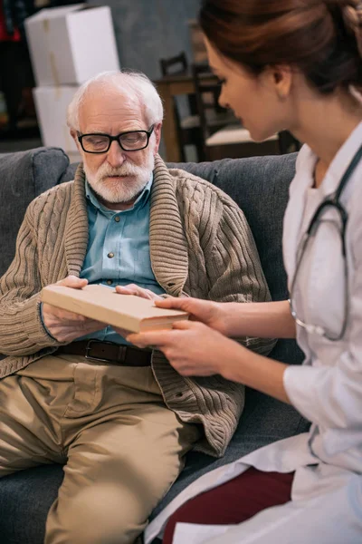 Uomo anziano prendendo libro dal medico femminile — Foto stock