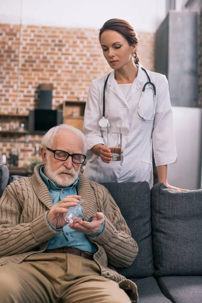 Лікар дає склянку води старшому пацієнту з таблетками — стокове фото