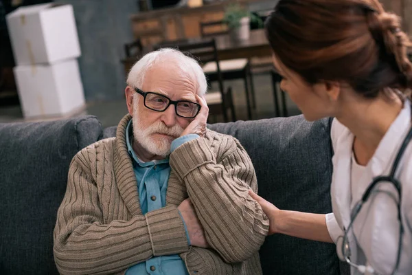 Hombre mayor deprimido mirando al médico femenino - foto de stock