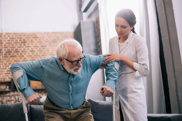 Doctor holding old male patient with crutches — Stock Photo