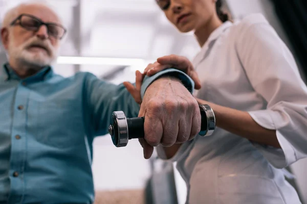 Close-up view of doctor holding senior man hand with dumbbell — Stock Photo