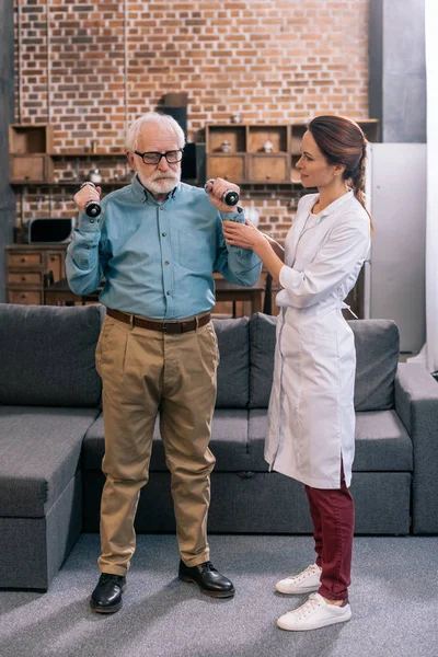 Doctor helping senior man exercising with dumbbells — Stock Photo