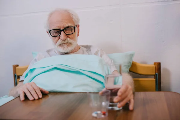 Hombre mayor paciente en cama clínica tomando medicamentos - foto de stock
